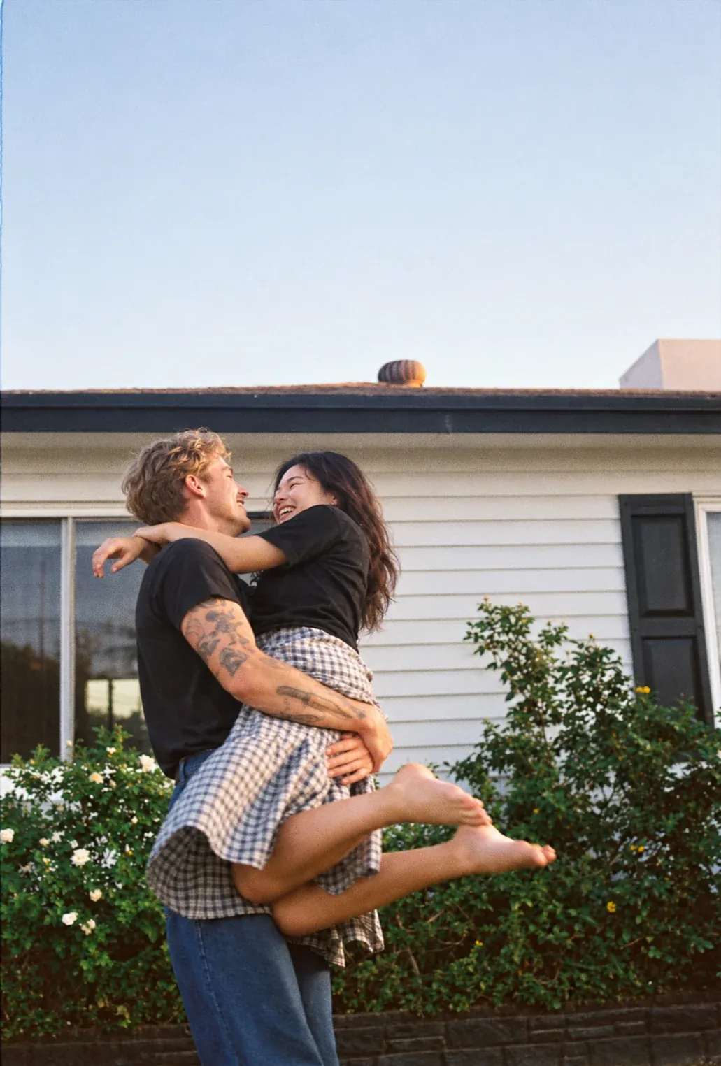 A man lifting his partner in a hug outside their house